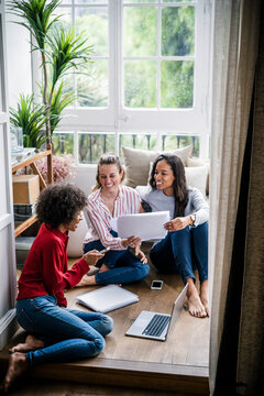 Three women with laptop, cell phone and documents sitting on the floor at home