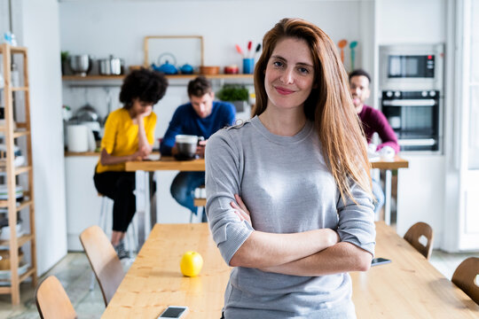 Portrait of woman at dining table at home with friends in background