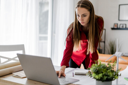 Woman in office working on plan and laptop with wind turbine model on table
