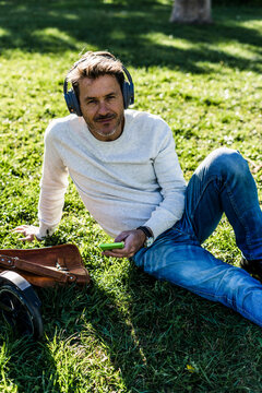 Casual businessman taking a break in a prak, sitting on grass, listening music