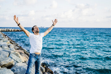 Man with raised arms and eyes closed standing in front of the sea