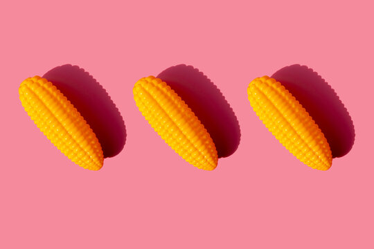 Studio shot of three plastic corn cobs against pink background