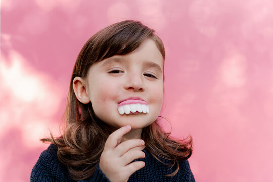 Portrait of little girl with false candy teeth in front of  pink background