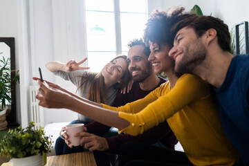 Four happy friends sitting on couch taking a selfie