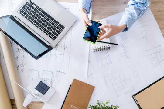 Close-up of woman in office using cell phone with plan, laptop and wind turbine model on table