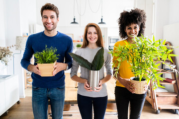 Portrait of three smiling friends holding plants at home