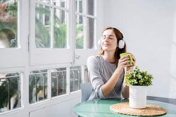 Young woman stting at the window at home with coffee cup and headphones