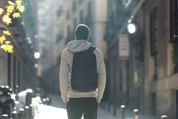 Man carrying backpack while standing with hands in pockets in city - obrazy, fototapety, plakaty