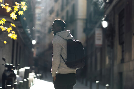 Young man with backpack looking away while standing on street in city
