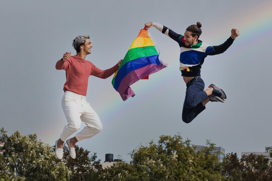Smiling men with scarf jumping against rainbow in clear sky