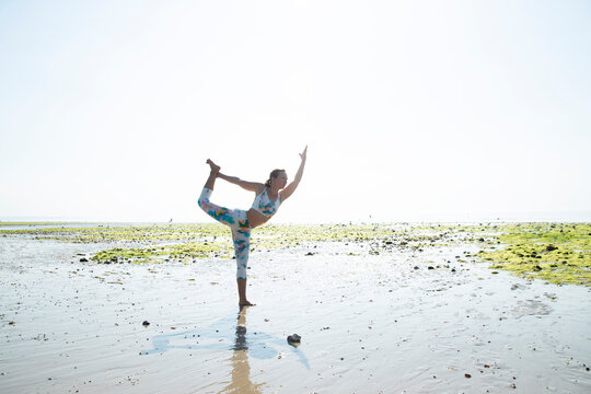 Mature woman practicing yoga at beach against clear sky