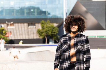 Curly hair man wearing open button shirt standing at skateboard park