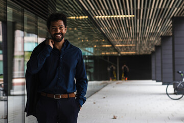 Smiling entrepreneur with hand in pocket holding blazer in city