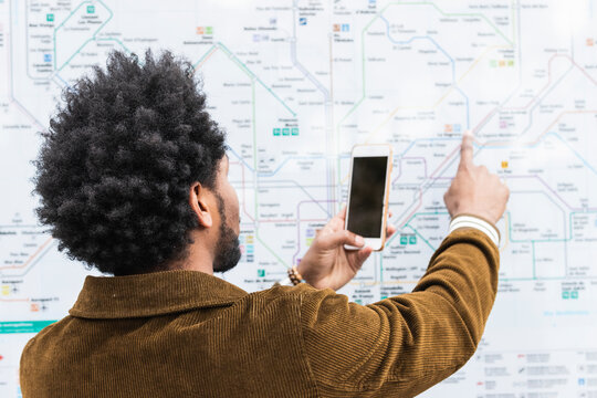 Man with afro hair using smart phone while analyzing map