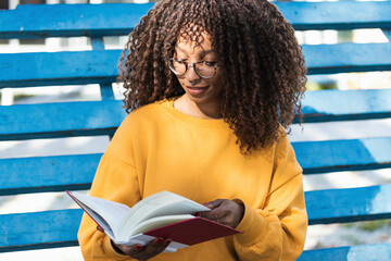 Smiling young woman reading book while sitting in bleachers