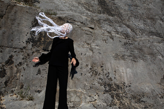 Woman dressed in black wearing crocheted white headdress with fringes shaking her head