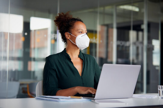 Portrait of businesswoman wearing  protective mask working on laptop at counter looking at distance