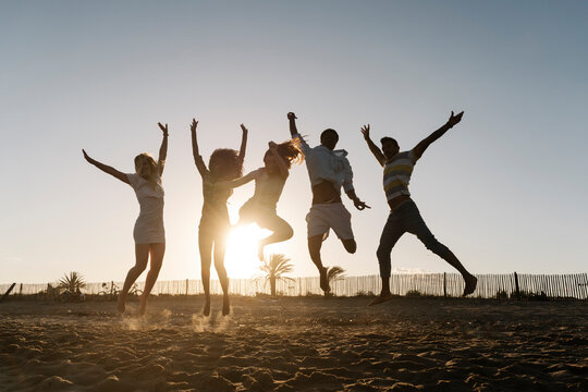 Friends jumping with joy on beach during sunset