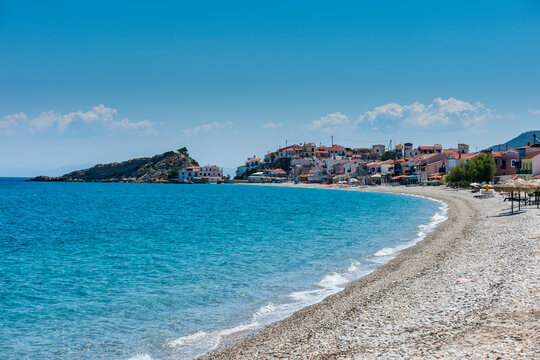 Greece, North Aegean, Kokkari, Rocky coastal beach in summer with village in background
