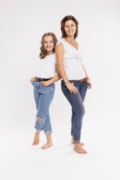 Smiling Mother And Daughter With Hands In Pockets Posing While Standing Against White Background