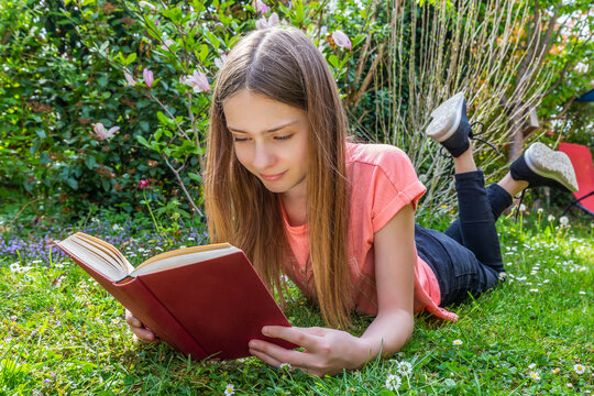 Girl lying on meadow reading a book