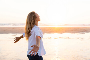 Carefree woman with arms outstretched looking up while standing against sea