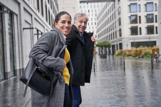Smiling business couple looking away while standing on footpath