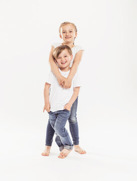 Portrait of smiling girl and her younger brother standing in front of white background