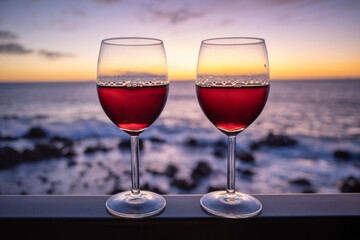 Two glasses of red wine with sea at sunset in background