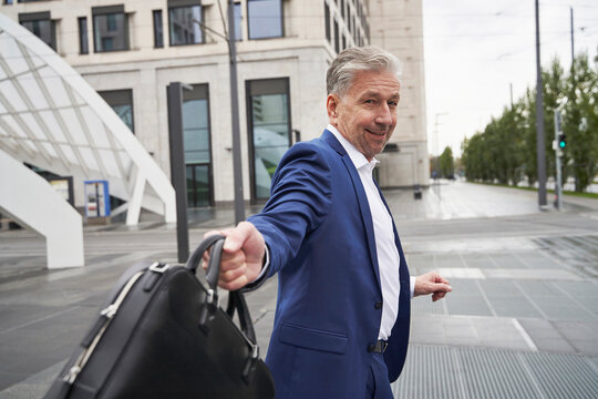 Happy Senior Businessman Holding Laptop Bag In City