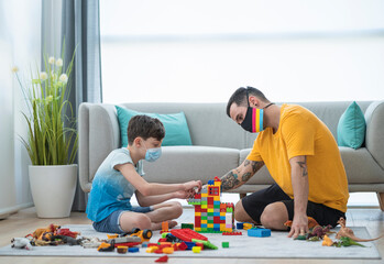 Man and boy wearing masks while arranging toy blocks in living room during curfew