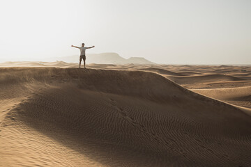 Mid distance of male tourist standing with arms outstretched on sand dunes in desert at Dubai, United Arab Emirates