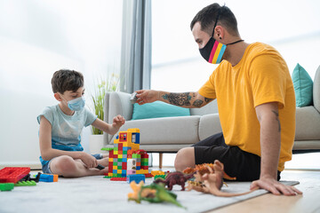 Man and boy wearing masks while playing with toy blocks in living room during Covid-19 curfew