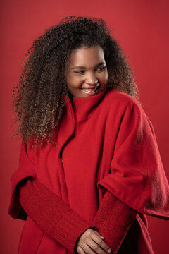 Smiling young woman wearing warm clothing looking away while standing against red background