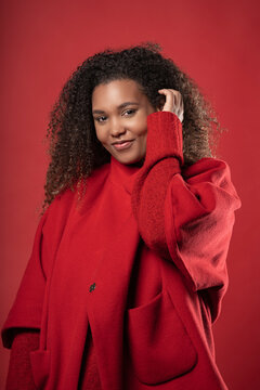Smiling woman with curly hair wearing coat while standing against red background