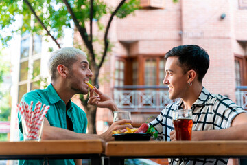 Smiling gay man feeding partner while sitting at bar counter in restaurant