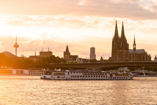 Germany, North Rhine-Westphalia, Cologne, Setting sun illuminating tourboat approaching Deutz Suspension Bridge