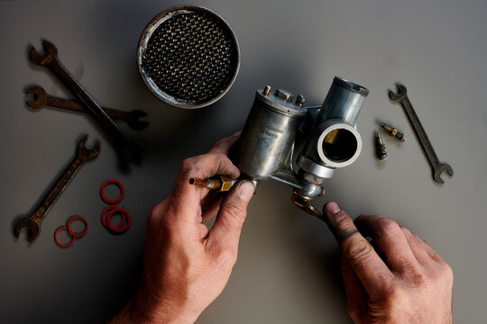 Top view of hand with vintage carburetor and tools in front of grey background