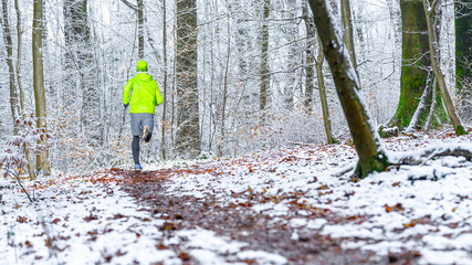 Young male athlete in green sports clothing jogging in forest during winter