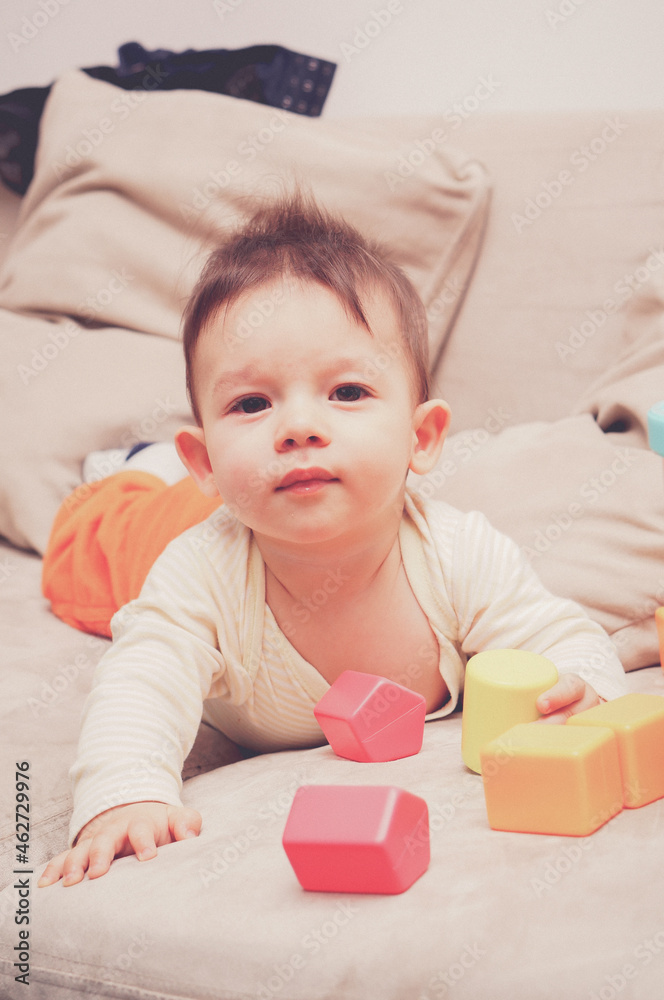 Sticker closeup of an adorable little boy playing with plastic colorful cubes while resting on the sofa