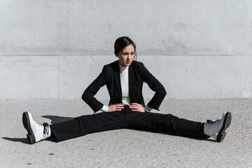 Young woman wearing black suit sitting on floor in front of concrete wall