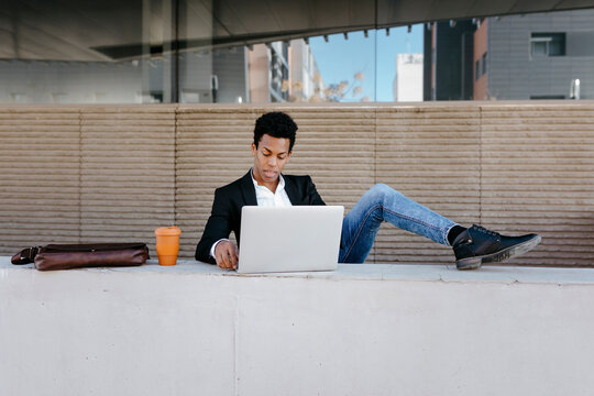 Businessman with feet up using laptop at retaining wall