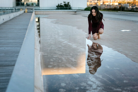 Young woman watching her reflection in a puddle