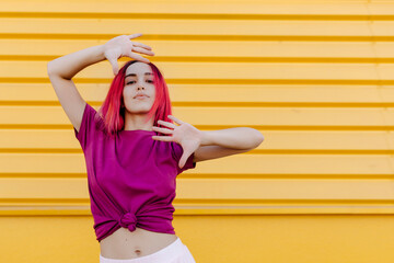 Confident young woman with dyed hair dancing against yellow wall
