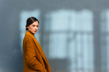 Woman wearing yellow winter coat while standing by gray wall