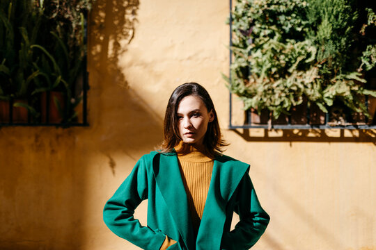 Beautiful Woman Wearing Green Jacket Standing Against Building In City On Sunny Day