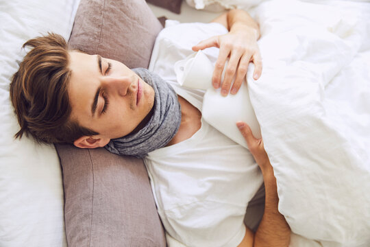 Close-up of sick young man with hot bottle sleeping on bed at home