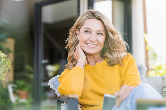 Portrait of smiling mature woman sitting on terrace with digital tablet looking at distance