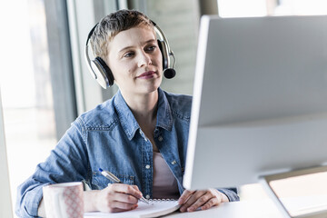 Businesswoman wearing headset at desk in office taking notes