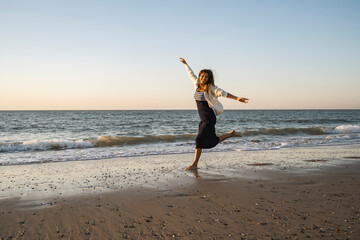 Carefree woman running at beach against clear sky during sunset